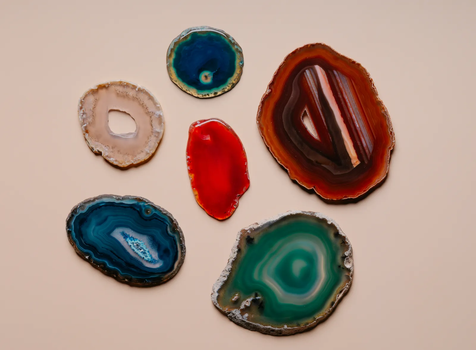 Six polished agate slices in blue, green, red and amber laid out on a beige background