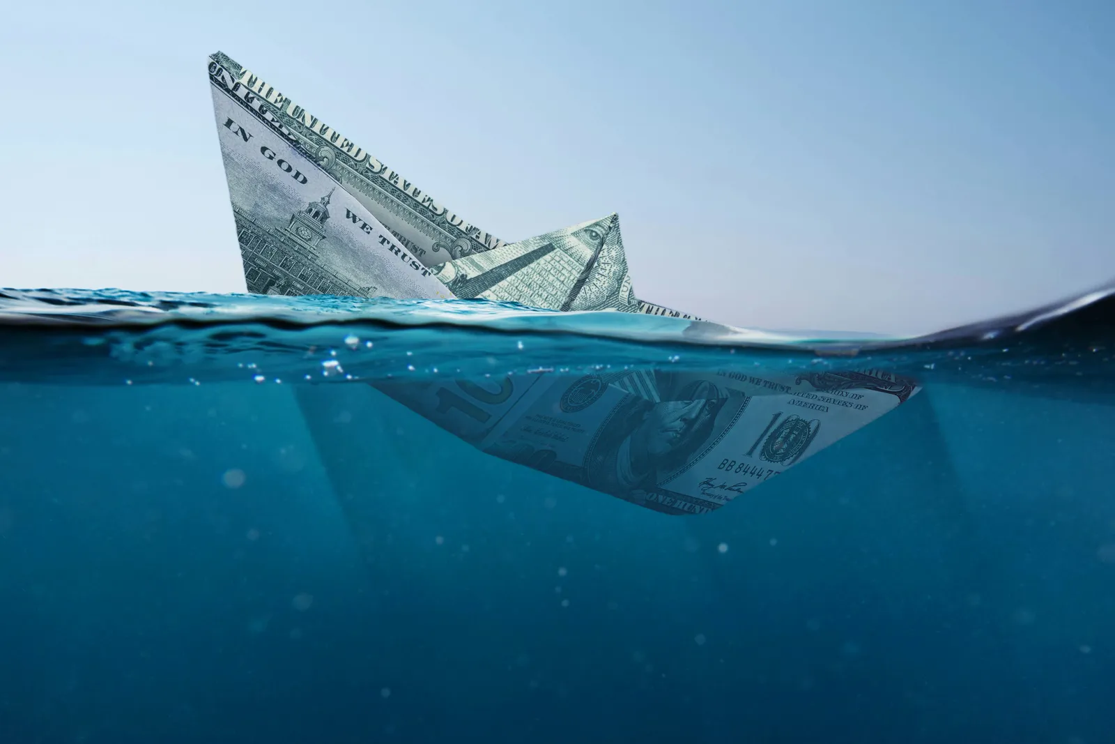 Paper boat folded from a dollar bill half submerged in clear blue water