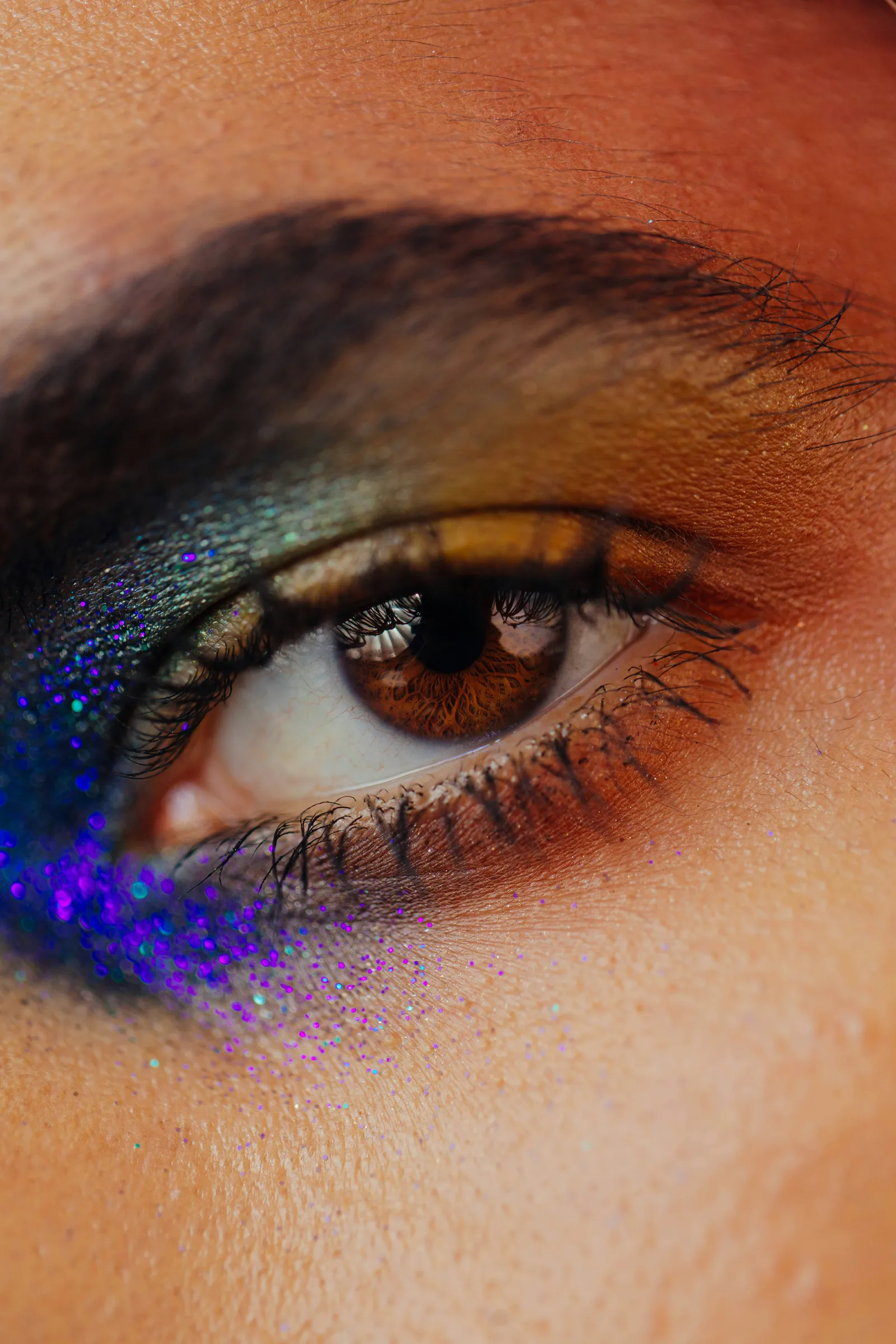 Extreme close-up of a brown eye with dark green and purple glitter eyeshadow
