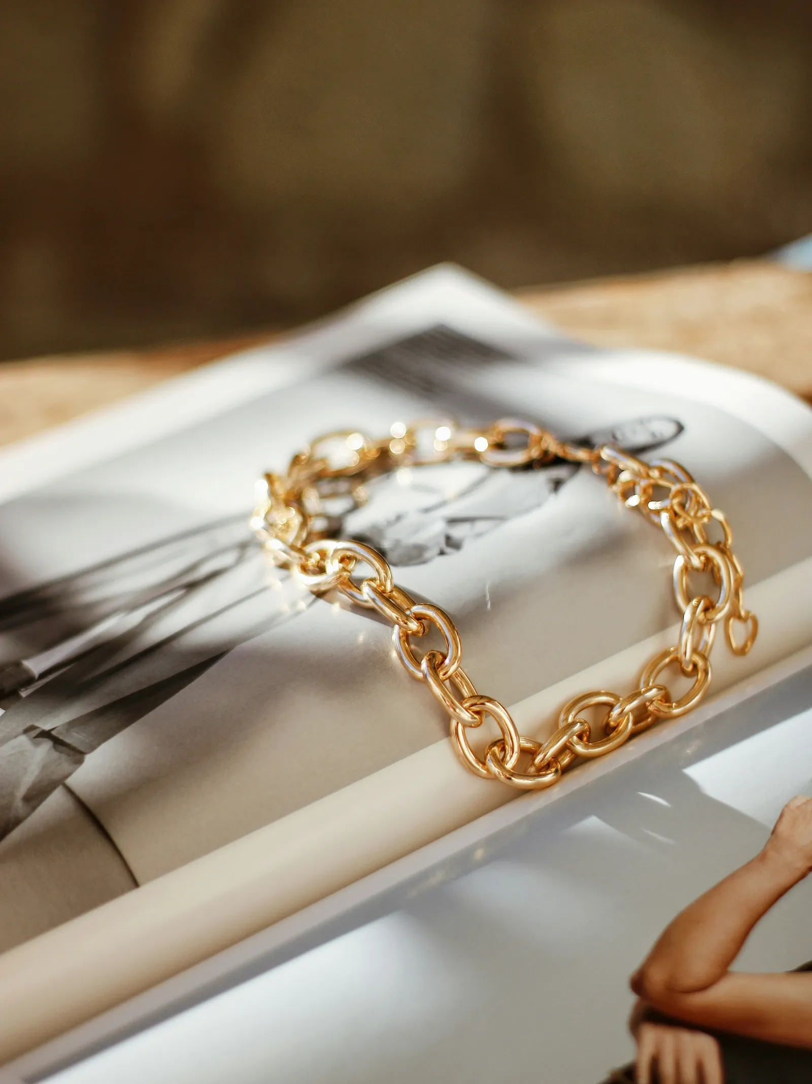 Chunky gold chain bracelet lying on an open fashion magazine in warm light