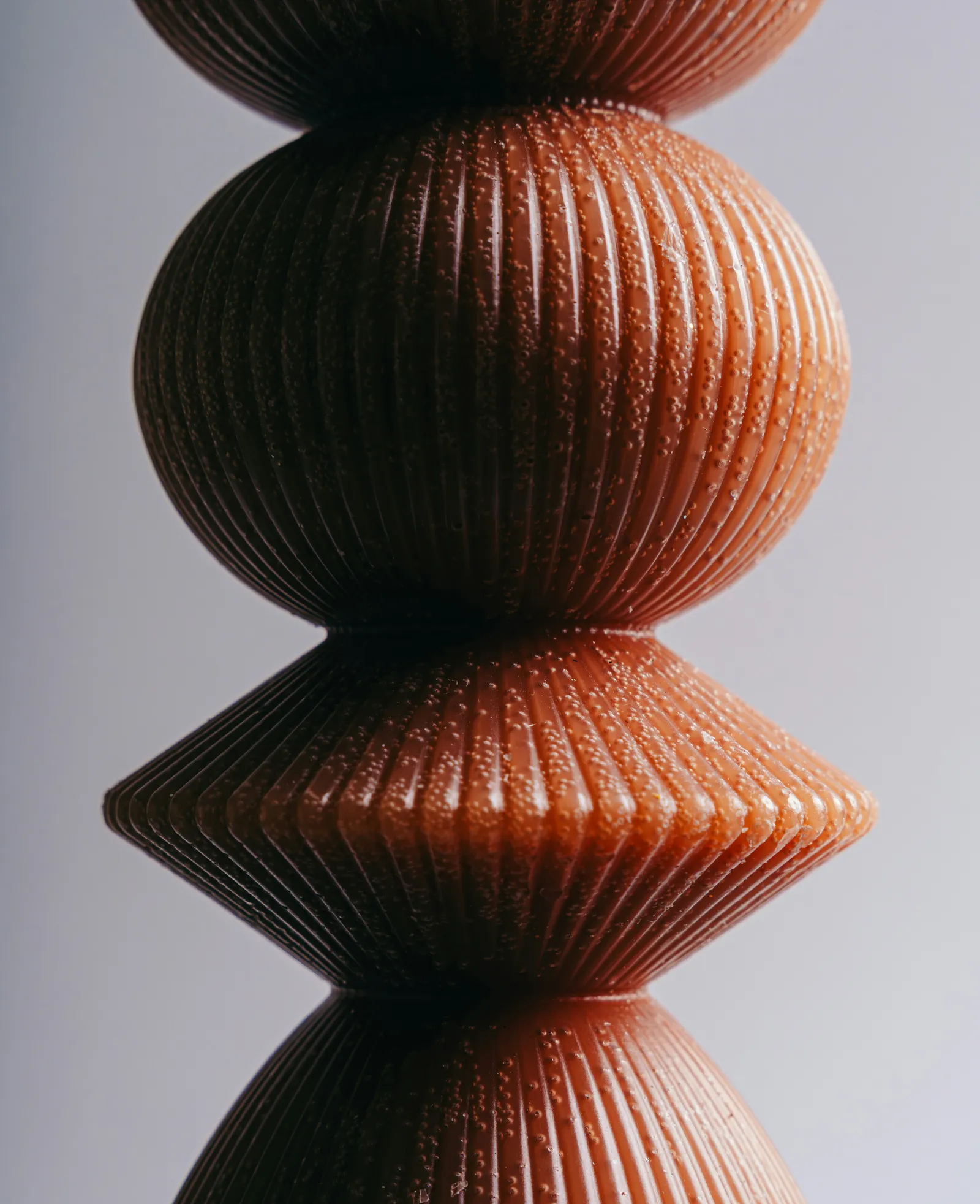 Close-up of a stacked ribbed terracotta object with round and conical shapes against a soft grey background