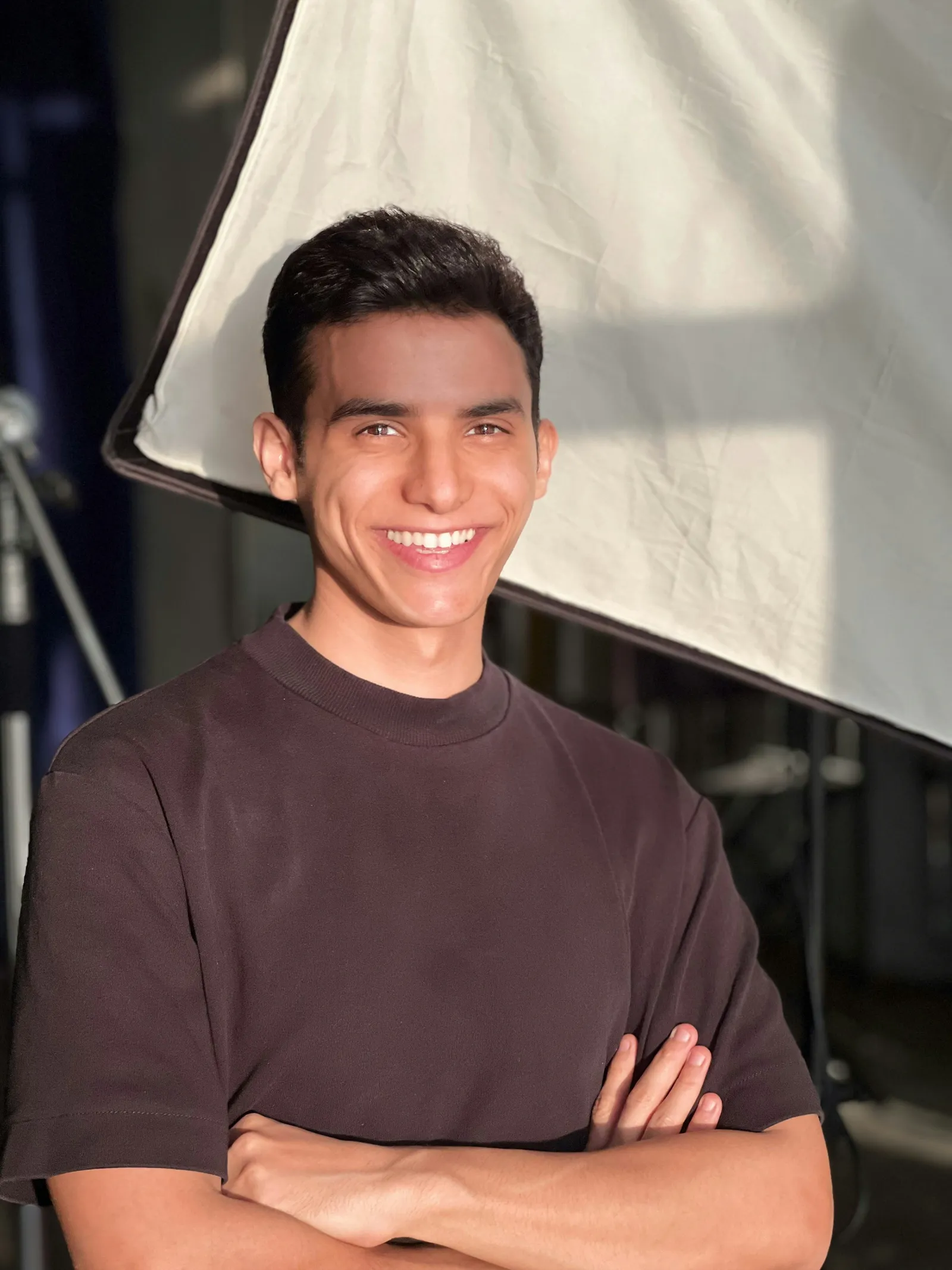 Smiling young man with arms crossed in a dark t-shirt standing in front of a large photography softbox