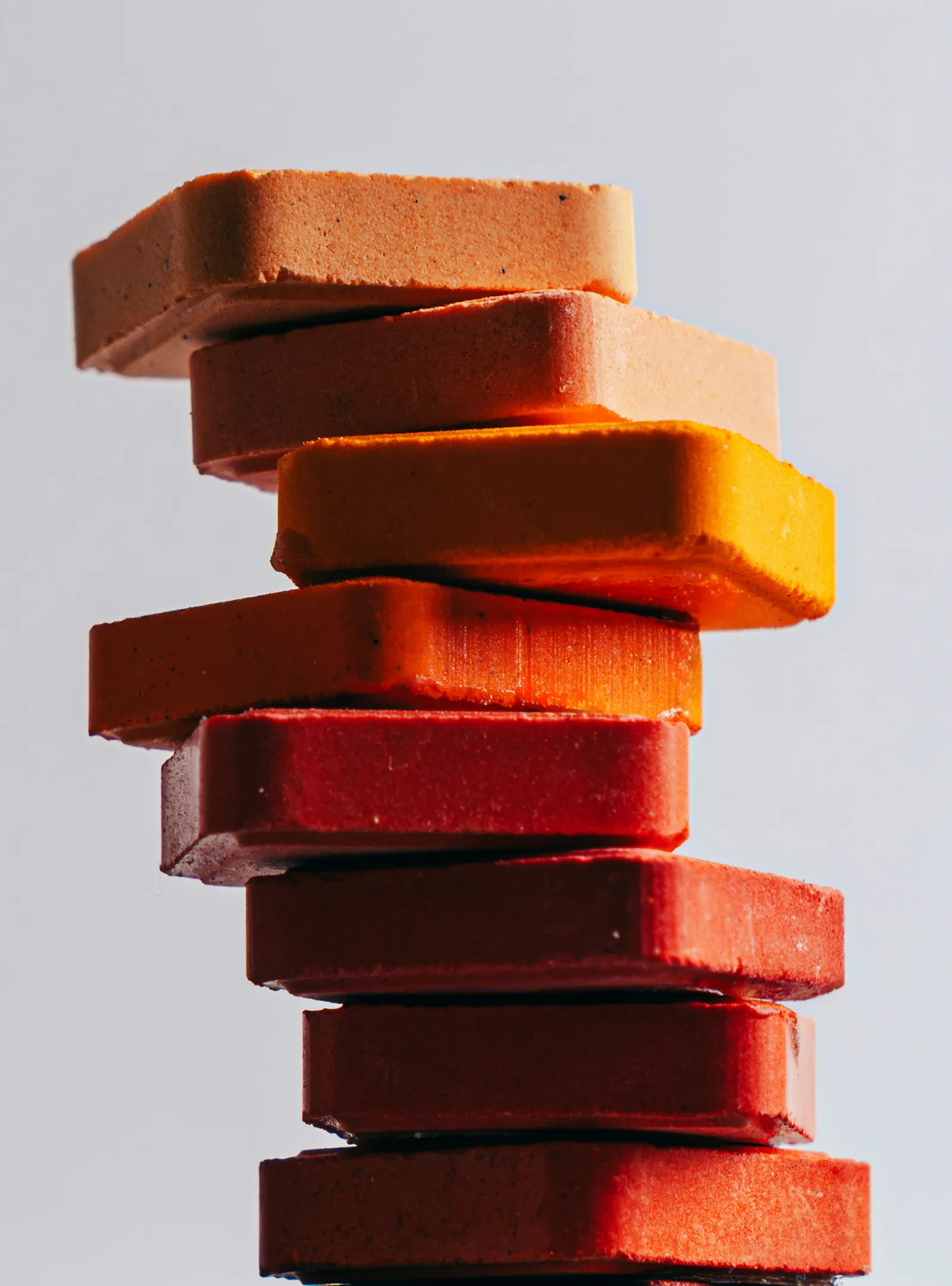 A tall stack of square soap bars in orange, coral and red shades against a light grey background