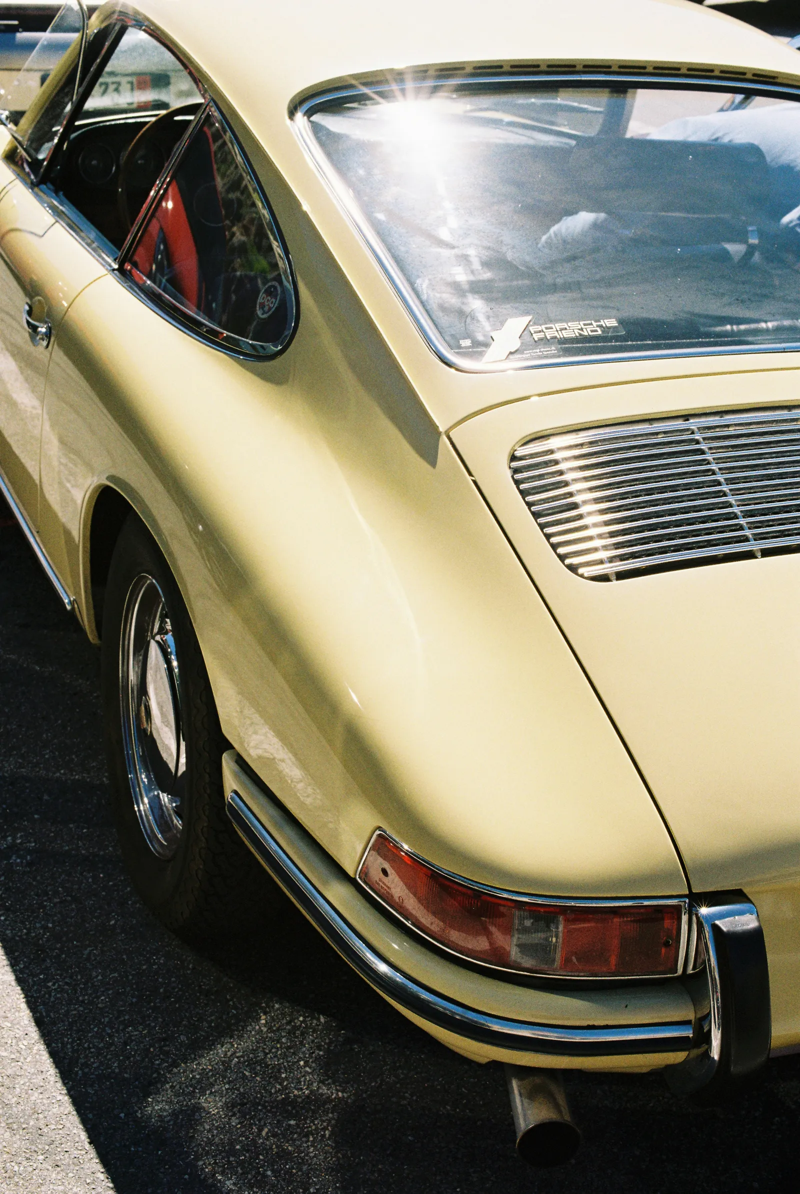 Rear quarter view of a pale yellow vintage sports car with a chrome bumper and red tail light, shot on film